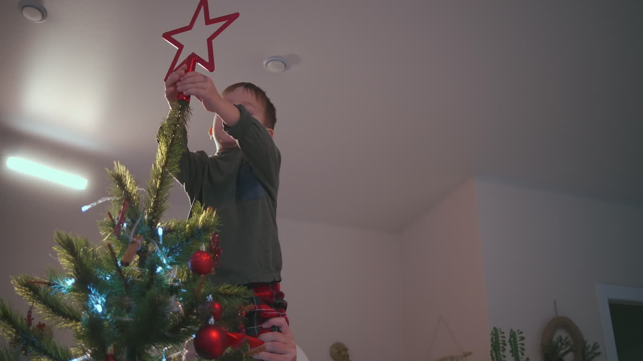 un niño coloca una estrella en la parte superior de un árbol de navidad. imágenes de alta calidad en 4k