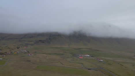 Aerial-view-of-Iceland-countryside-landscape,-Small-houses-on-green-meadow,-Foggy-mountain