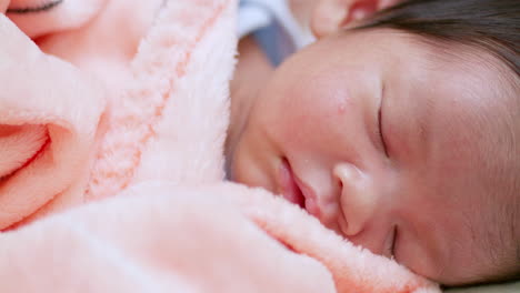 panning from the left to the right on a blurry shot of a sleeping newborn child that is wrapped in a soft, pink blanket