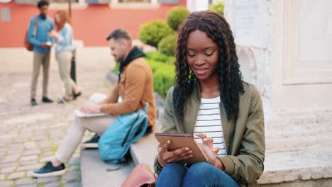 African-american-woman-using-a-tablet-while-sitting-on-the-ground-in-the-street