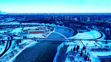 winter aerial forward flyover the north saskatchewan towards the walter dale bridge as round ice pieces go down river at a birds eye view reflection of buildings on the shoreline snow covered parks2-3