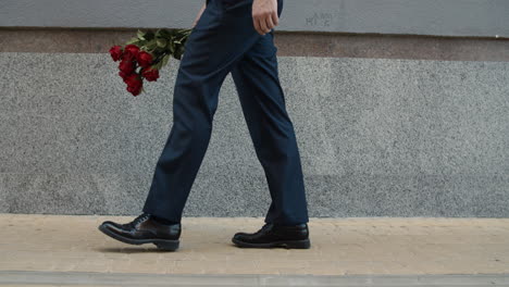 Closeup-man-carrying-roses-at-street.-Man-holding-red-roses-in-hand-at-street