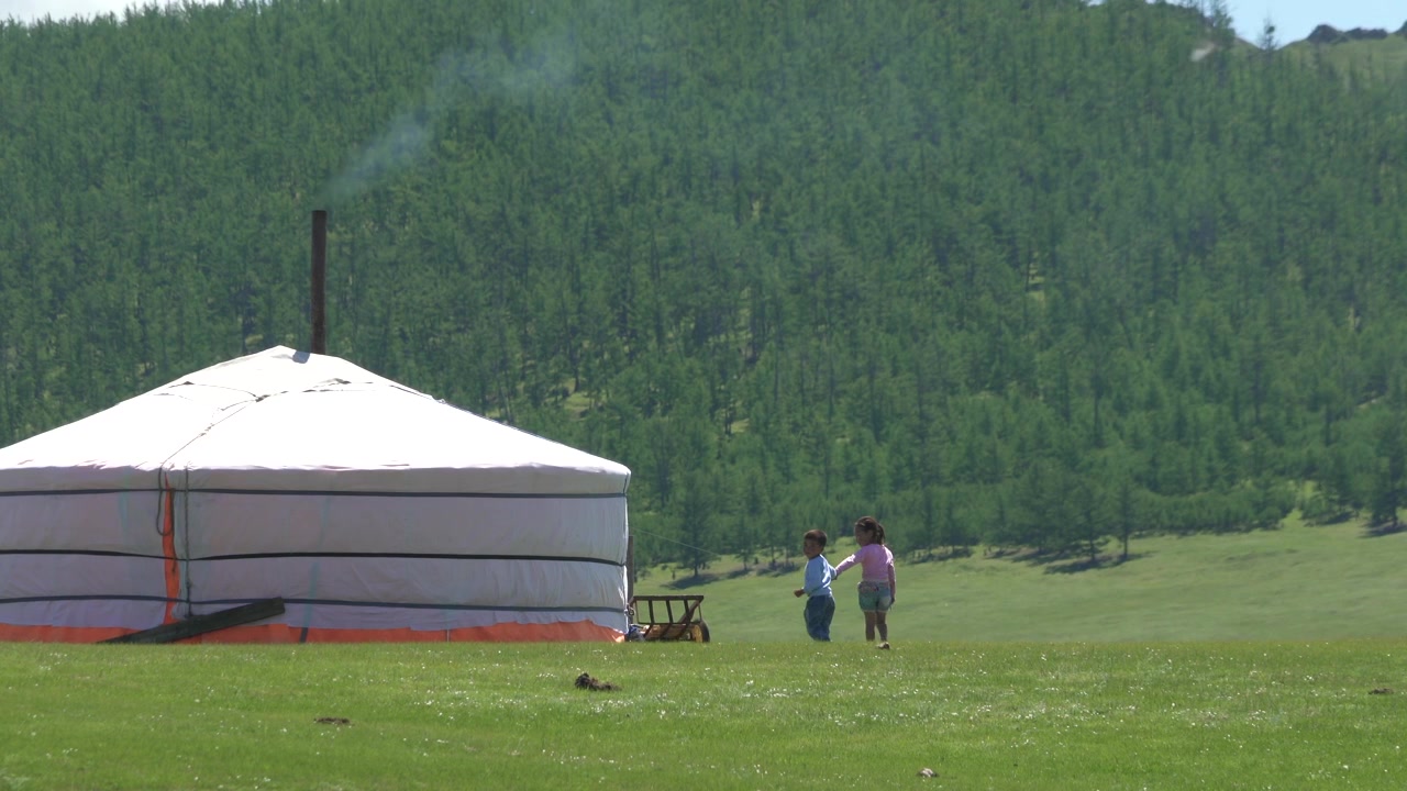 Två barn håller hand och går nära en traditionell mongolisk jurta