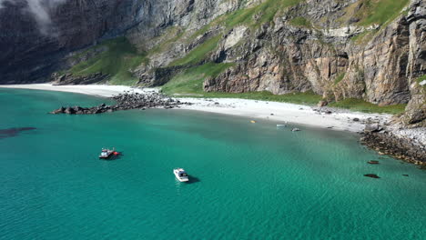Aerial-footage-of-a-boat-in-clear-blue-waters-at-the-island-of-Vaeroy,-Lofoten-Islands-in-Norway