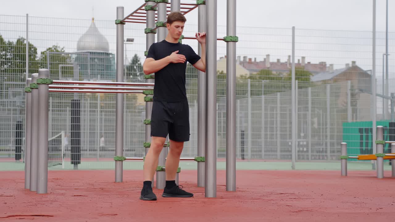 Wide view of man holding onto workout bar while stretching beside sports field or track
