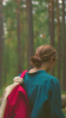 vista de atrás de jóvenes excursionistas colgando bolsas sobre sus hombros en un bosque sereno, mujer de camisa verde sostiene bolsa roja con envoltura de tela, mientras que su compañero, con un bandana azul, está cerca