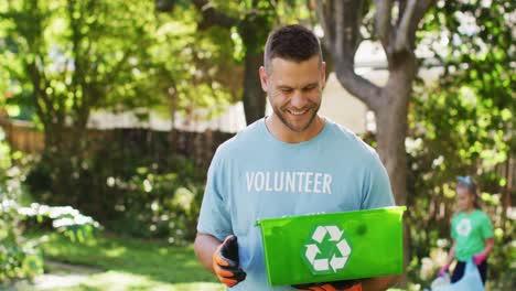 hombre caucásico sonriente con camiseta de voluntario sosteniendo una caja de reciclaje, recolectando residuos plásticos