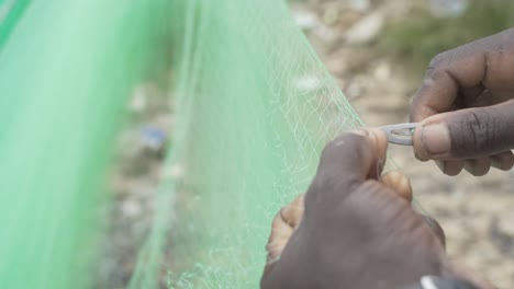 African man's hands mending a fishing net