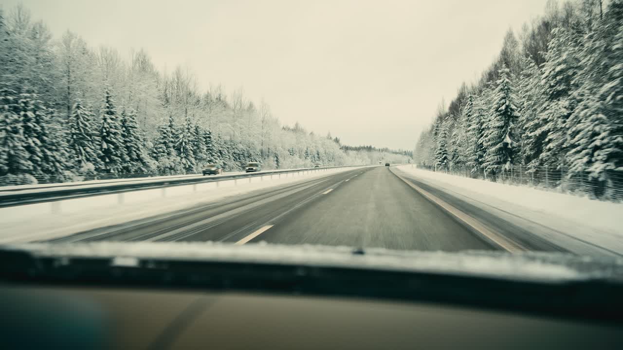 Point of view driving along a winter highway with snow covered trees, empty road and overcast sky. Smooth forward motion captures cold weather travel, transportation, seasonal landscape and quiet jour