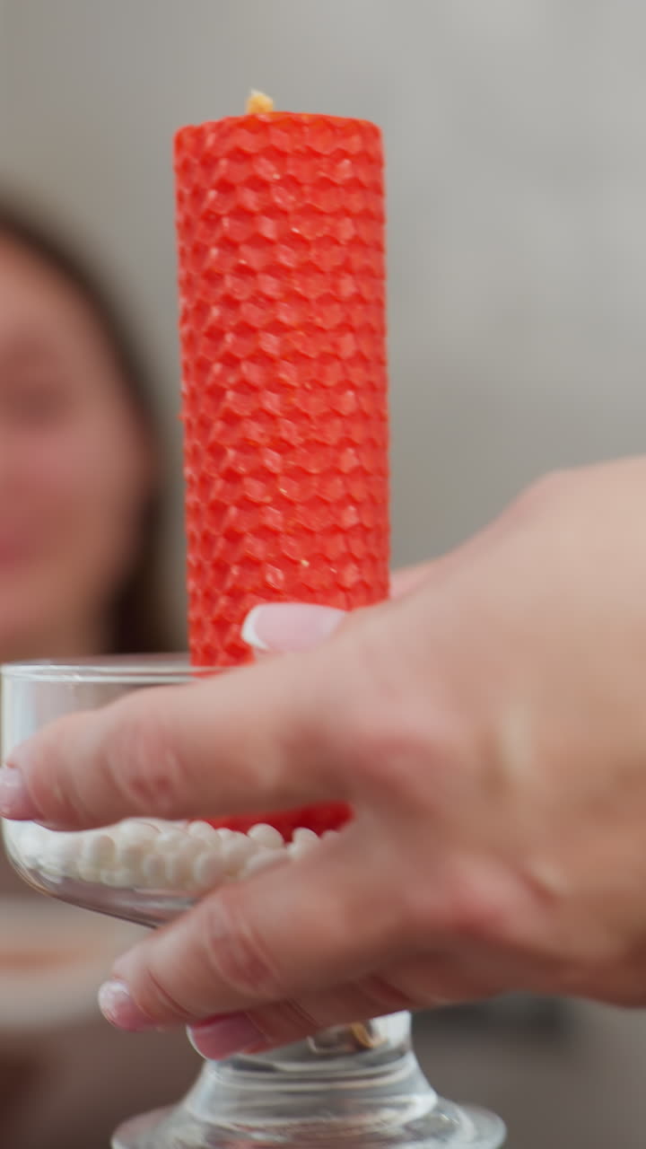 primer plano de una mujer colocando delicadamente una elegante vela roja en un soporte de vidrio en la mesa mientras se prepara para el desayuno, la mano adornada con un hermoso brazalete de cuentas