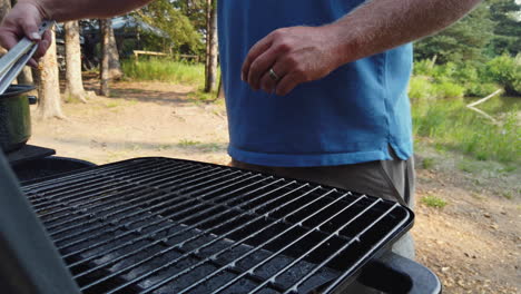 caucasian man grilling big juicy beef steaks on barbecue while camping