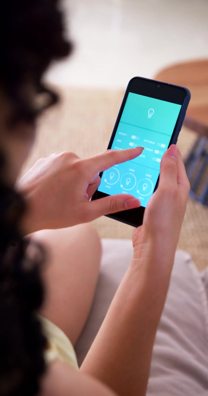 Adult female sitting on sofa holding phone responding to lightbulb icon and adjusting 3 dials