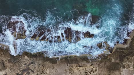 Top-Down-View-Over-A-Rocky-Shore-Line-In-Malta,-With-Waves-Splashing