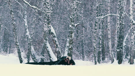 modelo con traje de fénix negro cae sobre la nieve en el bosque de invierno