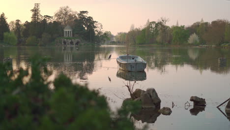 a static shot of an abandoned boat in the middle of the lake of the vincennes woods parc at sunset in paris, france