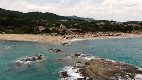 azure waves crashing in towards beautiful luxury resort down by golden beach covered in sunbeds