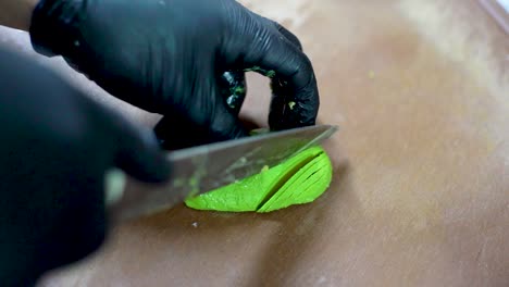 chef hands cutting green avocado on a wooden cutting board, top view