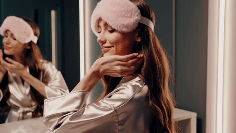 woman in satin robe with sleep mask applying skincare