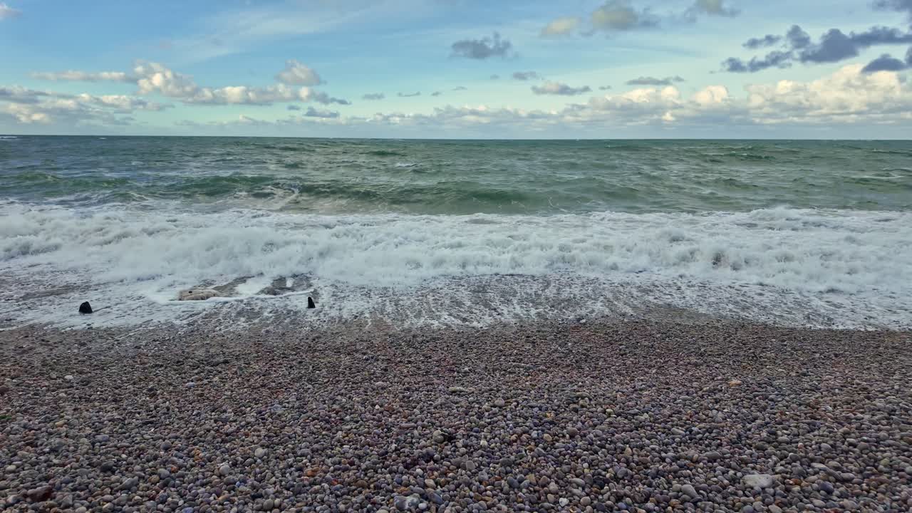 Bølger i slowmotion ruller ind på rullestensstranden i Étretat, Normandiet i Frankrig.