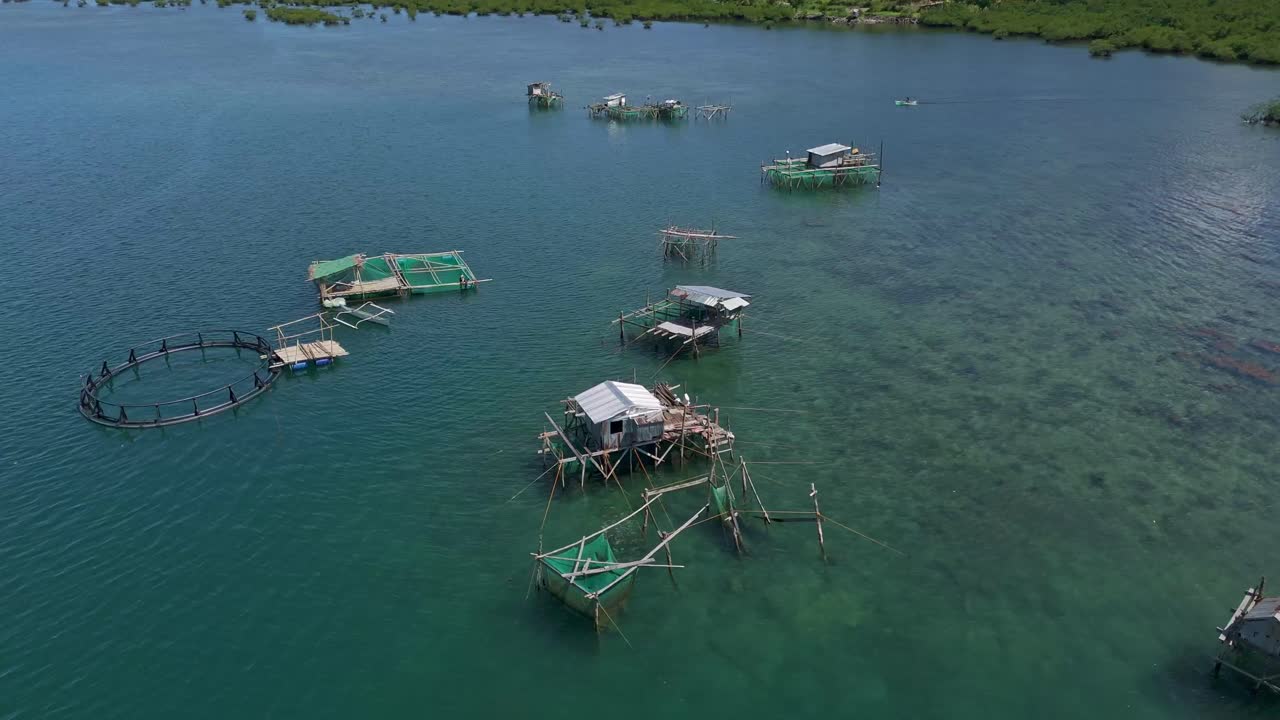 A group of fishermen's huts on stilts, over shallow turquoise water close to a lush shoreline