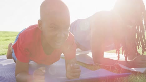 Video-of-happy-african-american-son-and-father-doing-plank-on-grass-on-sunny-day