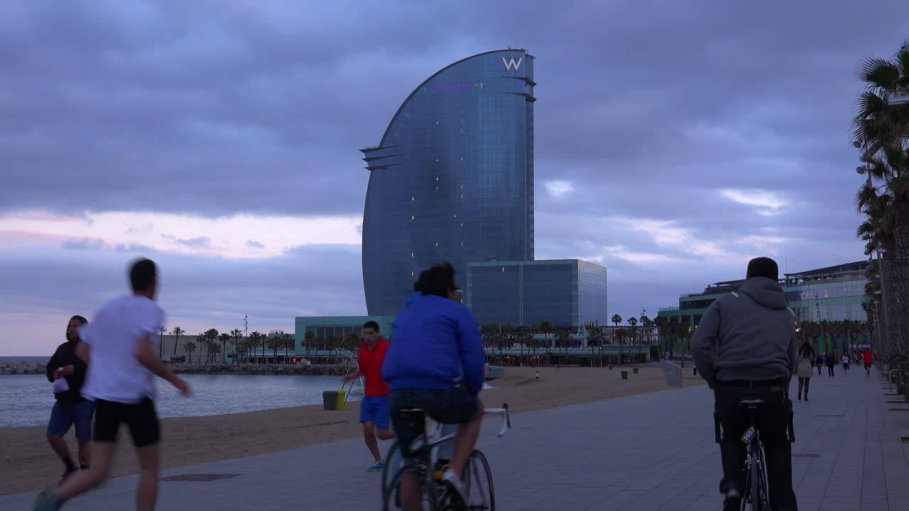 스페인 바르셀로나의 해변을 따라 산책로를 따라 자전거와 조깅하는 사람들이 이동합니다.