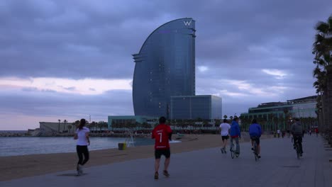 Los-Ciclistas-Y-Corredores-Se-Mueven-A-Lo-Largo-De-Una-Pasarela-A-Lo-Largo-De-La-Playa-En-Barcelona,-España