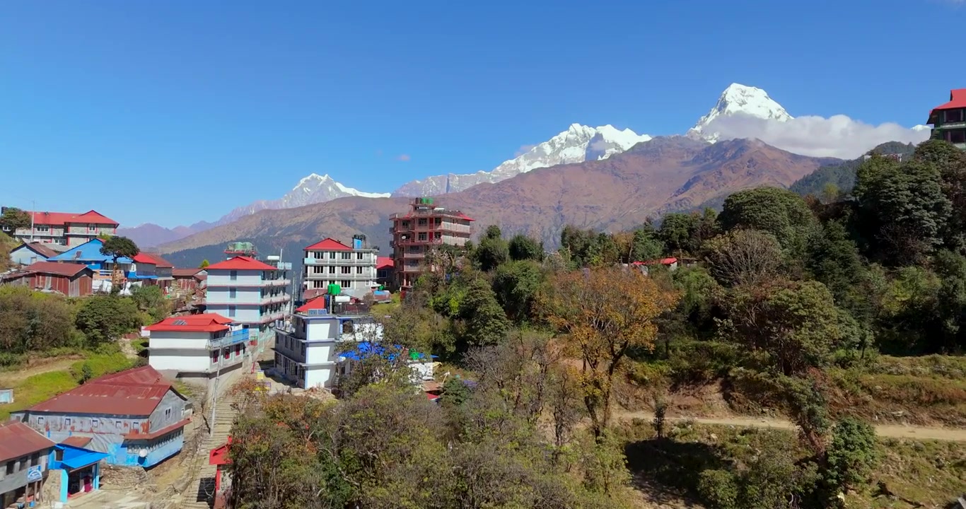 Annapurna Region, Ghorepani, Nepal, drone advancing over colorful village rooftops and lodges toward snow-capped Himalayan peaks in the background