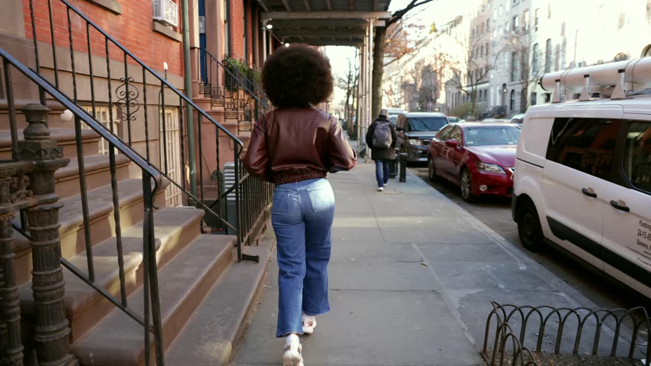 Mujer caminando por una calle de la ciudad con casas de piedra rojiza.