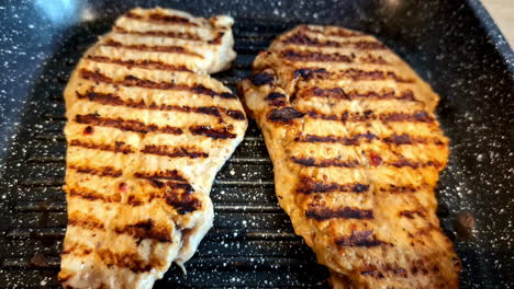 two grilled chicken breasts sizzle on a hot non-stick pan, showing defined sear marks