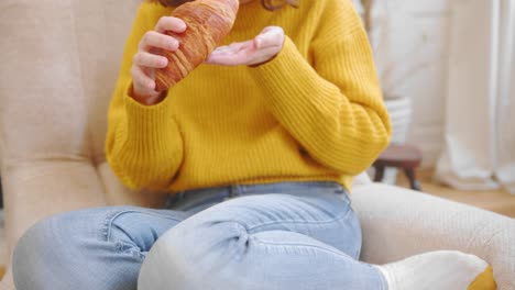 casual woman eats delicious croissant on couch, front view