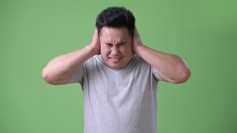 young handsome overweight asian man against green background