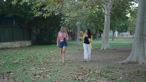 two young women walking and talking in a park