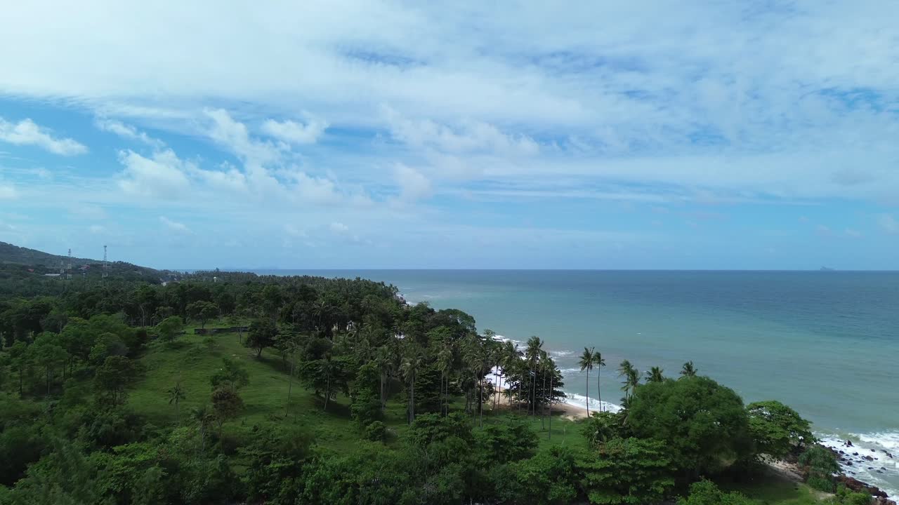 Scenic aerial footage of Koh Lanta, Thailand, showing a remote tropical coastline with lush palm trees, crystal clear turquoise water, rocky shore and hidden beaches in the distance