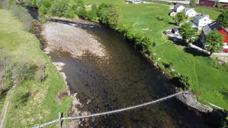 Flying-over-old-wooden-suspension-bridge-crossing-Dale-river---Famous-Norwegian-salmon-fishing-river---Aerial-following-downstream