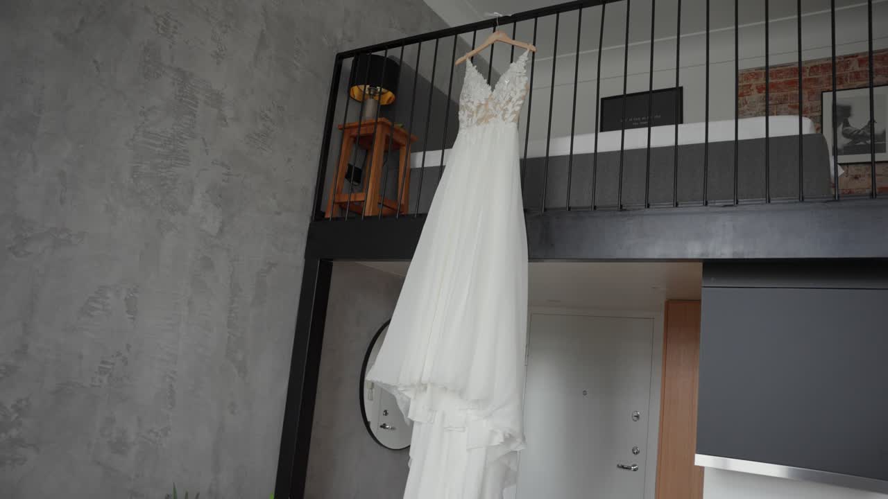 A detailed view of a wedding dress hanging in a modern loft interior with textured walls and contemporary design, showcasing elegant craftsmanship and interior lighting