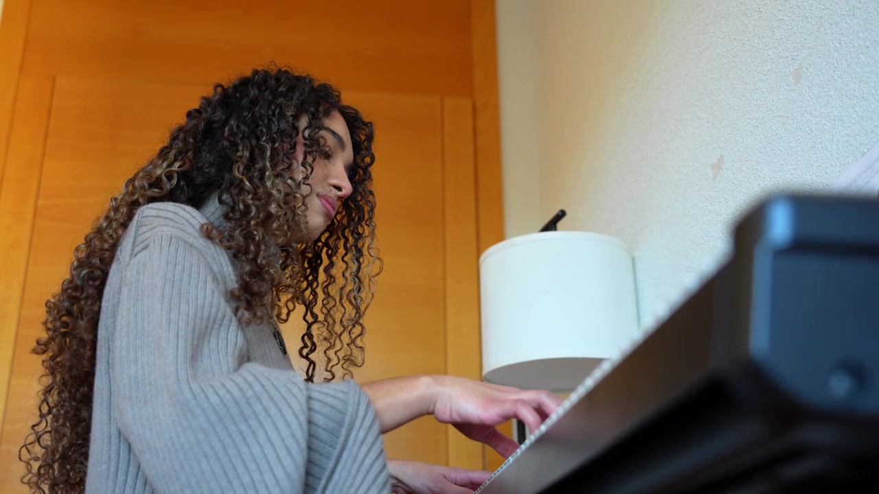 Young woman with curly hair playing a song on a digital piano in a cozy room