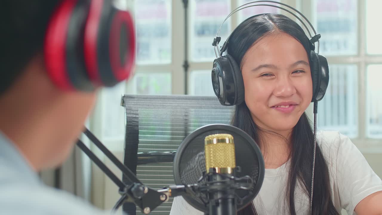 Over Shoulder View Of Asian Boy Host Record Podcast Use Microphone Wear Headphone Interview Guest Conversation For Content In His Home Studio. Content Creator Concept