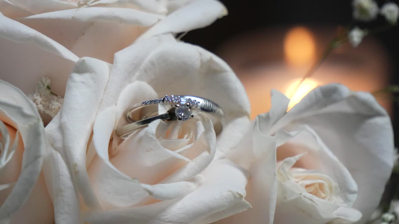 Two white gold wedding rings among the white rose petals of the bride's bouquet