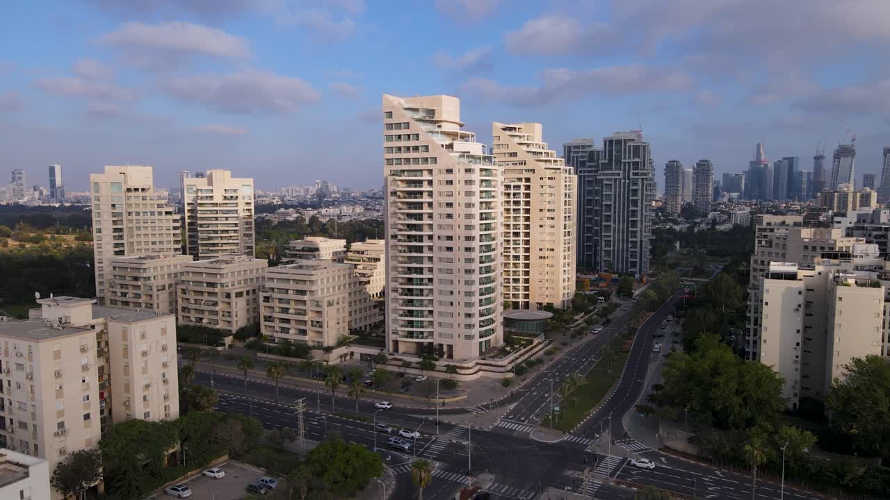 Drone ascends over sunny modern buildings and light traffic in Tel Aviv streets.