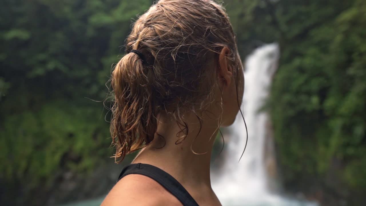Woman looking towards a Rio Celeste waterfall in the blurred background.The serene scene captures a moment of quiet contemplation for the raw beauty of nature at Rio Celeste