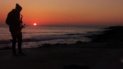 Umriss-Eines-Jungen-Männlichen-Musikers,-Der-Saxophon-Am-Meer-Unter-Einem-Glühenden-Sonnenuntergang-Mit-Kopierraum-Spielt