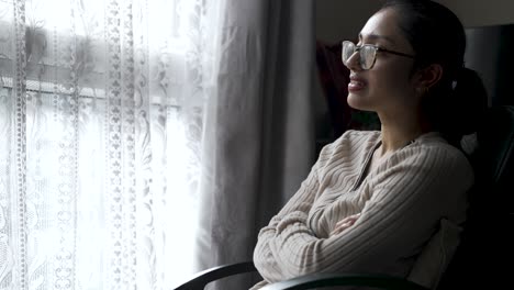 a person sits on a rolling chair in a household environment next to a window with curtains, gently pacing back and forth, reflecting in moments of introspection, captured in slow motion