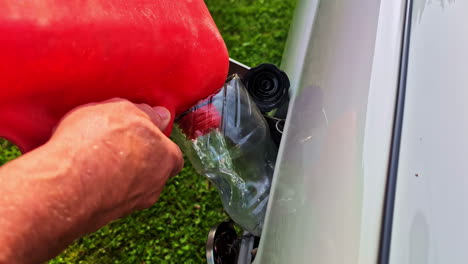 person pours gas using red fuel can and cut plastic bottle funnel into a small motor