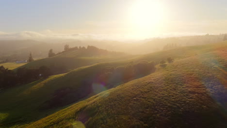 aerial cinematic view of hills with afternoon mist and golden hour sun rays in the evening