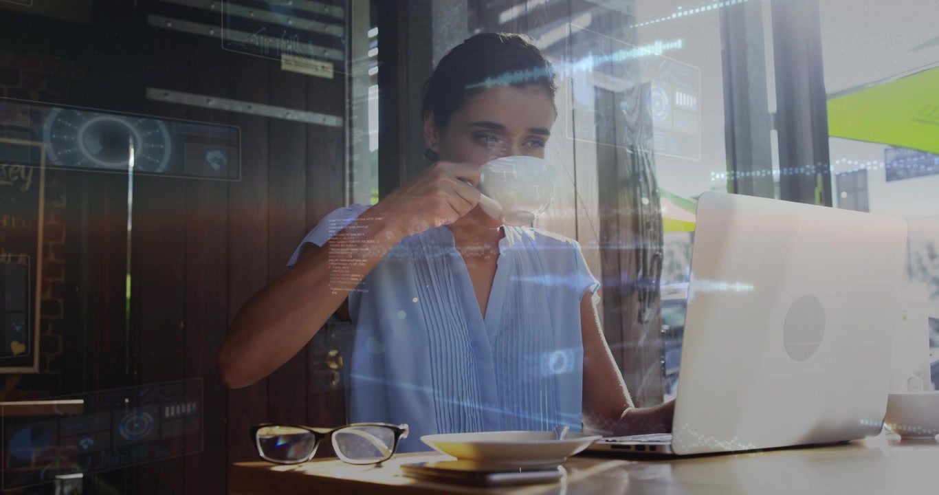 Donna che allunga la mano per prendere una tazza di caffè e fa apparire chiare sovrapposizioni di dati olografici mentre programma.