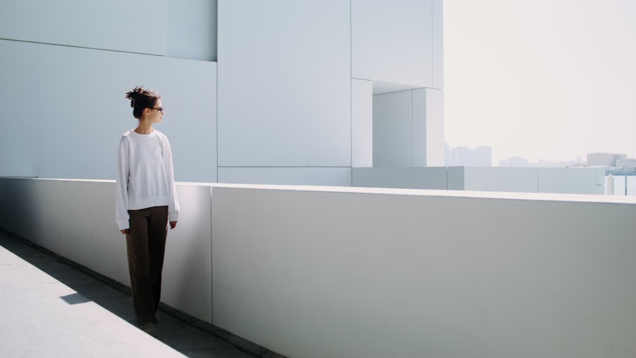 mujer con sudadera blanca y pantalones marrones en un entorno arquitectónico moderno