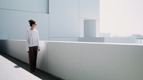 mujer con sudadera blanca y pantalones marrones en un entorno arquitectónico moderno