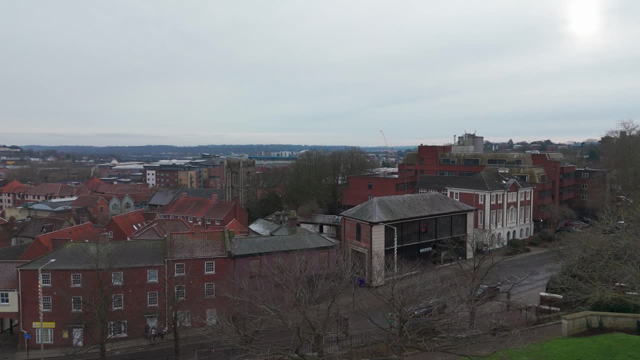 A quiet urban park with historic Norwich buildings and church towers visible outdoors