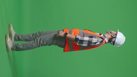 full body side view of asian male engineer with safety helmet looking around while standing in the green screen background studio